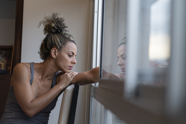 woman very sad and depressed by many things that lives in pajamas by the window with an attitude of pain and loneliness