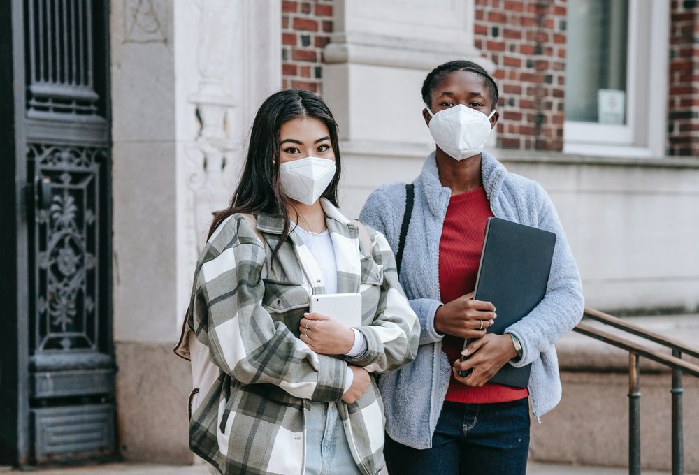 young female teenagers wearing masks while standing on stairs of university
