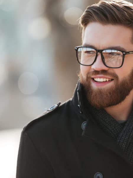Portrait of happy bearded young man in glasses standing outdoors