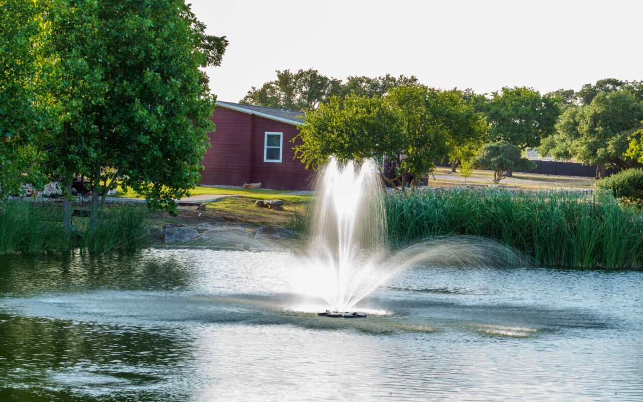 Outdoor water fountain feature surrounded by green trees and manicured landscaping