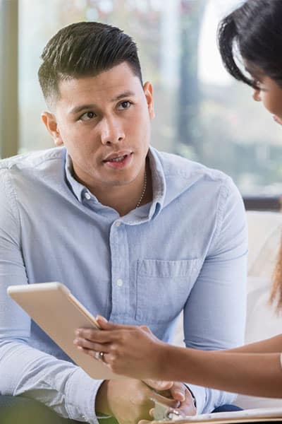 Man in a light blue shirt holding a tablet and looking directly at the camera