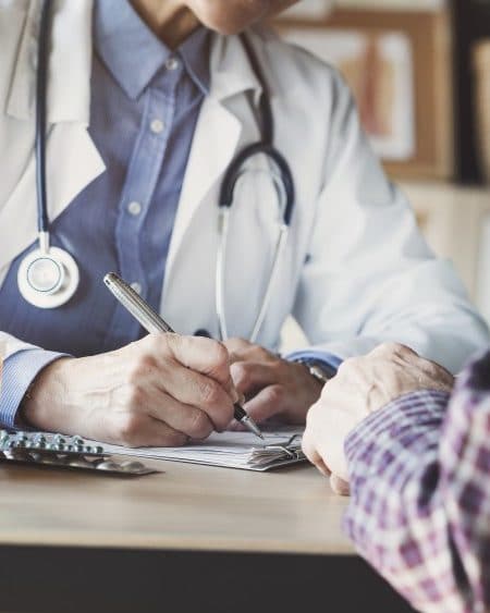 Healthcare provider with a stethoscope writing notes during a patient consultation