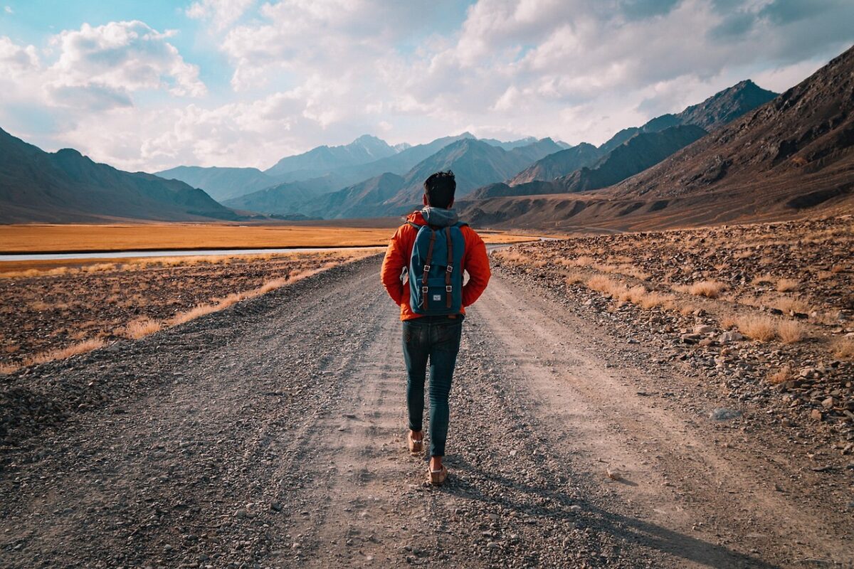 Person walking alone down a long straight desert road toward distant mountains
