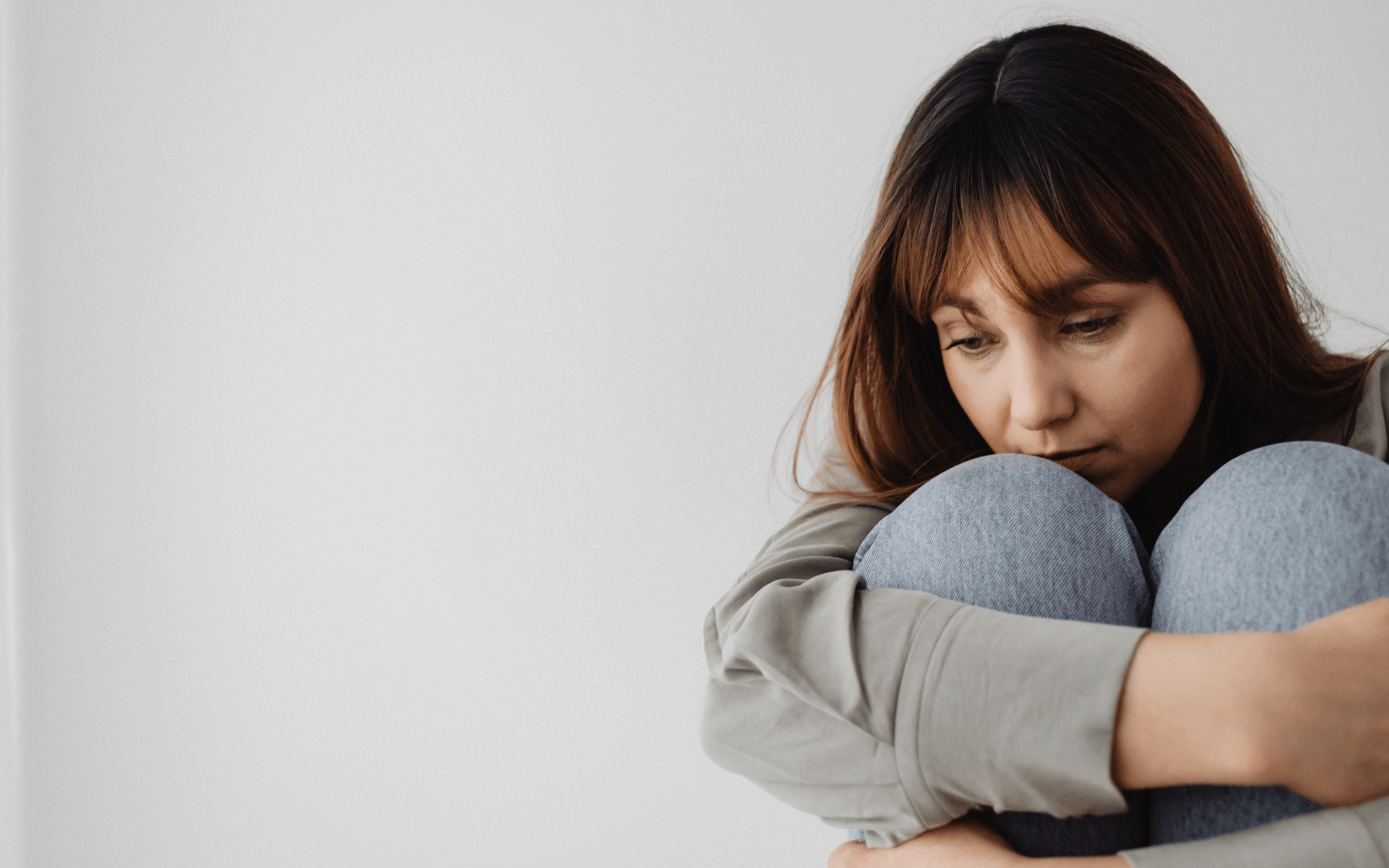 Young woman sitting with her knees pulled up and hand on her head looking overwhelmed
