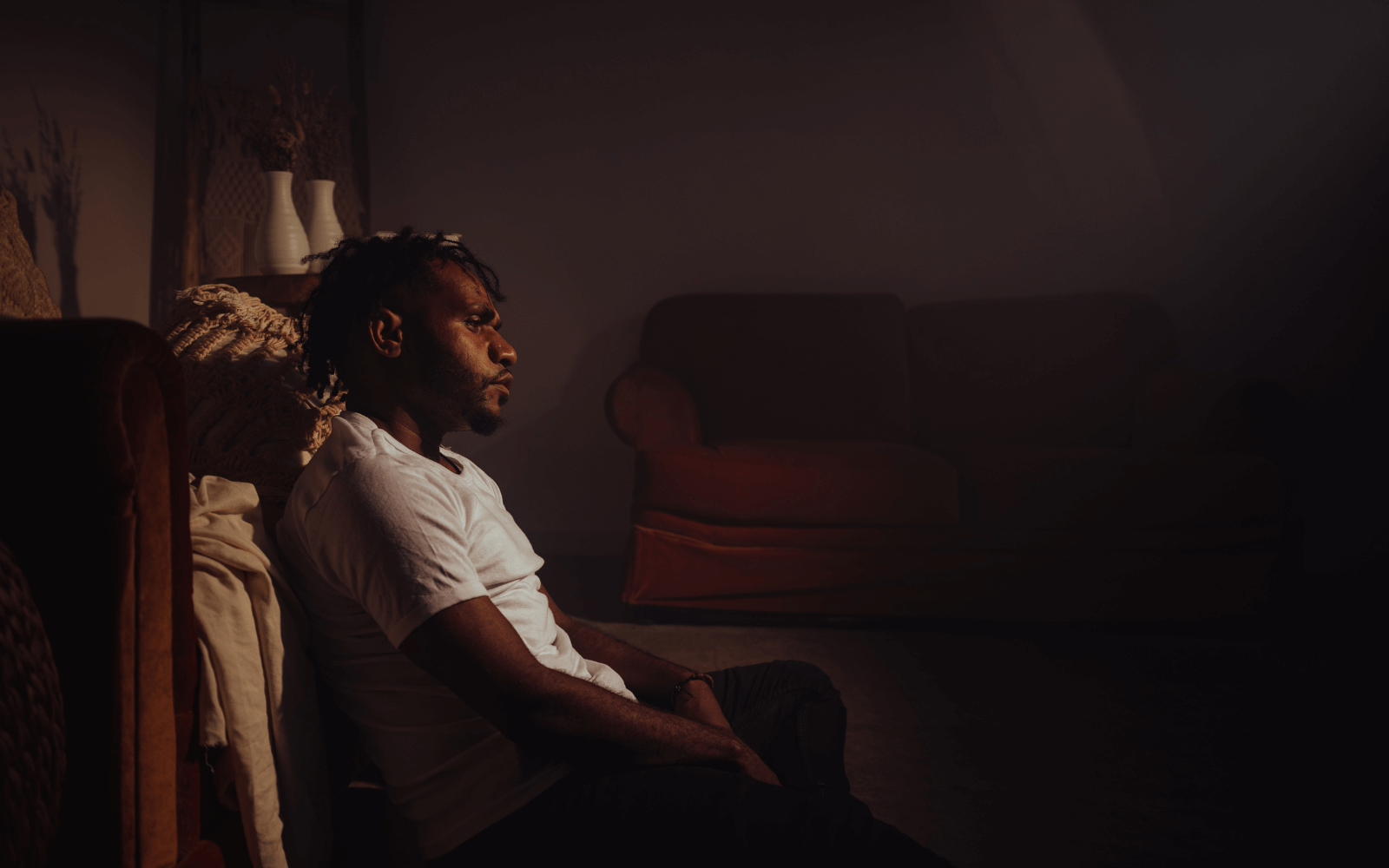 Person sitting alone in a dark room with their head down in a posture of distress