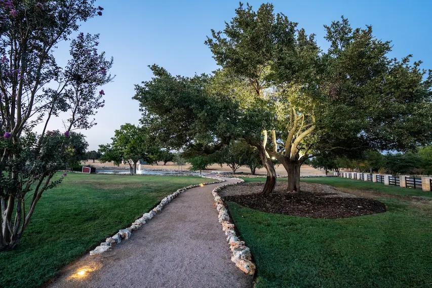 Curved stone pathway leading through landscaped grounds with large oak trees at Alta Loma.