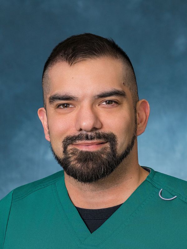 Man with short dark hair and a beard smiling against a dark blue background