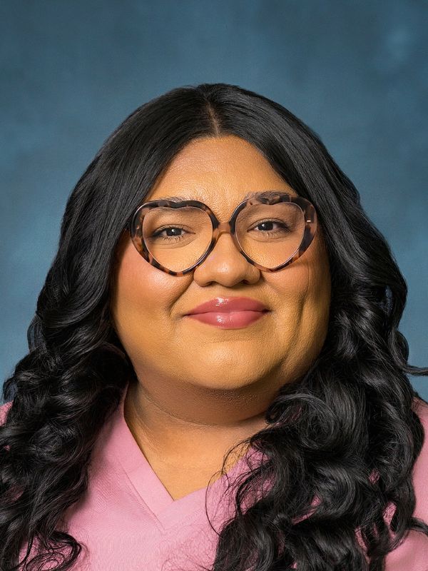 Woman with glasses and curly dark hair smiling confidently against a light background